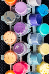 jars with remnants of paints for drawing and painting on a woolen black background in soft focus for the design of children's creative sites; vertical photo