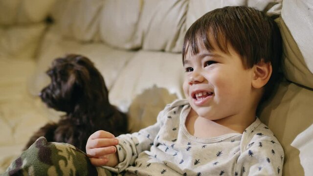 Cheerful Asian kid watching TV, smiling. A puppy is sitting next to him