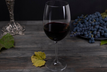 Composition with a glass of red wine and grapes on a dark background of gray wooden boards. Winemaking concept. Still life with wine in a dark key
