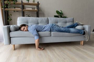 Exhausted young man fell asleep on comfortable couch in modern living room, having no energy after...