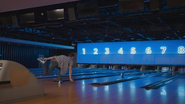 A young man in a bowling alley throws a ball in slow motion and knocks down skittles. Play bowling. Throw balls on the floor of the bowling club