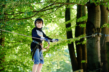 Two children in forest adventure park. Kids boys in helmet climbs on high rope trail. Agility...