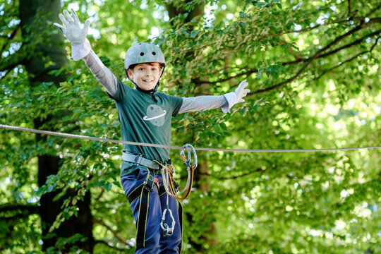 Two children in forest adventure park. Kids boys in helmet climbs on high rope trail. Agility skills and climbing outdoor amusement center for children. Outdoors activity for kid and families.