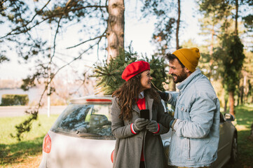 Happy young couple with their Christmas tree is standing in front of the car.