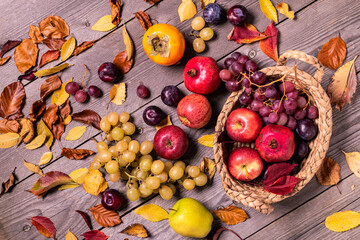 on a rustic wooden background a harvest of seasonal fruit and autumn colored dry leaves.