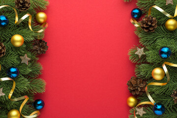 Top view photo of gold and blue small christmas tree balls pine cones stars and gold ribbon serpentine on pine branches on isolated red background with blank space