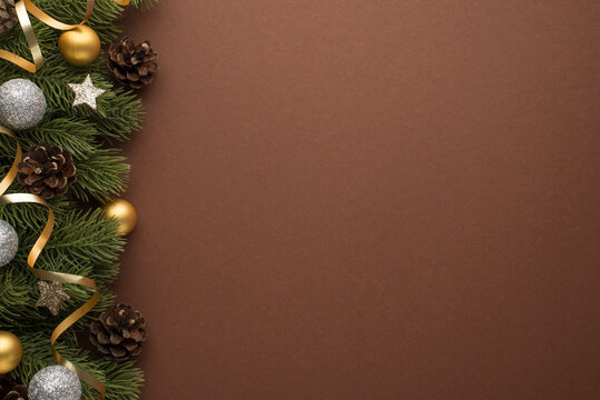 Top view photo of golden and glowing silver christmas tree balls cones stars and serpentine on pine twigs on isolated brown background with blank space
