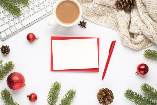 Top view photo of red envelope paper sheet pen keyboard cup of hot drinking red christmas tree balls pine twigs cones anise and cozy sweater on isolated white background with copyspace
