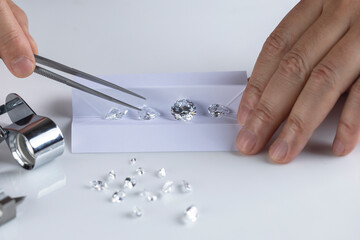 Close up of diamond expert's hand at workplace evaluating gemstones polished diamonds. High quality...