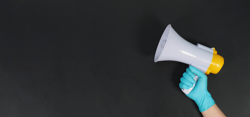 Megaphone in hand and wearing blue latex glove on black background. Studio shooting.