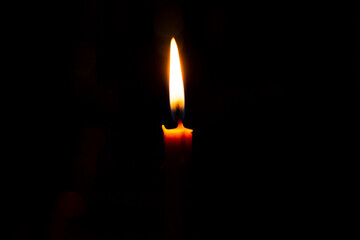 The flame on a yellow candle glows in the dark