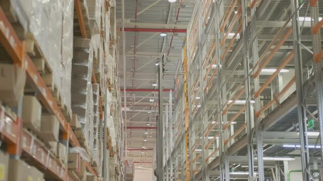 worker on forklift telescopic loader moves pallets with goods by lifting them onto shelf in storage warehouse.