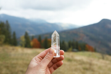 Woman holding beautiful crystal in mountains, closeup