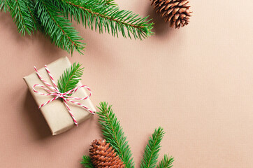 Christmas gift box with green fir tree branches with cones on beige paper background