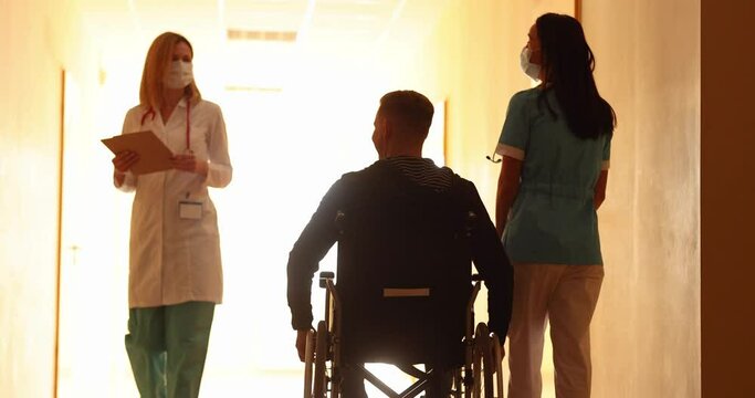 Nurse walking with disabled man in wheelchair along corridor of clinic and greeting doctor 4k movie