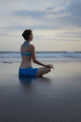 Fototapeta na wymiar Beach yoga practice in Bali. Lotus pose. Padmasana. Hands in gyan mudra. Meditation and concentration. Zen life. Relaxation of body and mind. Yoga retreat. View from back. Copy space.