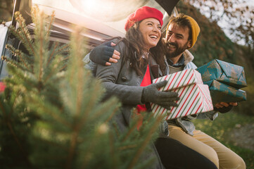 Attractive young couple in front of their car with Christmas presents