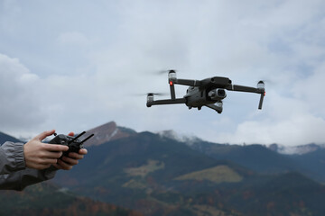 Woman operating modern drone with remote control in mountains, closeup