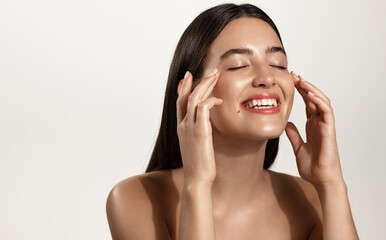 Smiling woman with clean glowing facial skin washing her face, rubbing in cream skincare product...