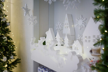 Christmas decorations. White wooden carved toys, reindeer, houses and fir trees. Branches with garlands. Soft focused shot.