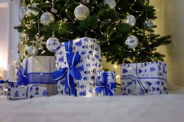 Christmas tree decorated with shiny garland and bulbs in white room. Wrapped present boxes, festive...