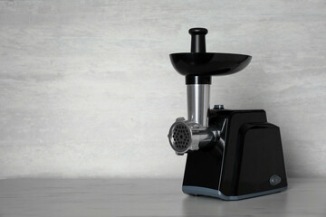 Modern electric meat grinder on light wooden table. Space for text
