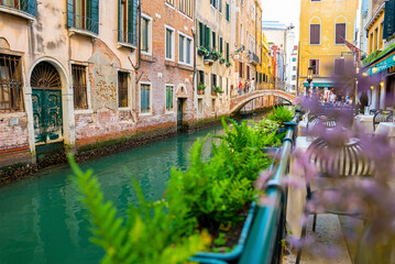 Pedestrians walking on bridge over narrow canal between residential building and open restaurant