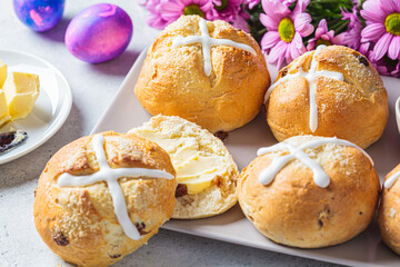 Traditional Easter cross buns with raisins on gray background with flowers and colored eggs.