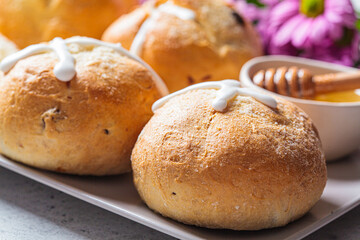 Traditional Easter cross buns with raisins with honey on a gray plate.