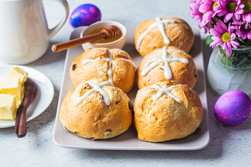Traditional Easter cross buns with raisins on gray background with flowers and colored eggs.