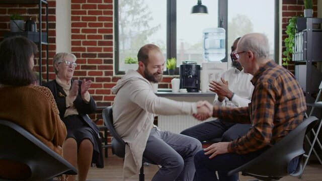 Man doing handshake with therapist and people after sharing addiction progress at aa meeting. Cheerful person celebrating therapy achievement and shaking hands with support group.