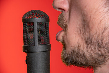 Singing Male Mouth In Front Of A Microphone On A Red Background. Broadcast, Radio and Podcasts. Singing Songs and Recording into the Microphone.