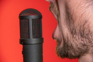 Singing Male Mouth In Front Of A Microphone On A Red Background. Broadcast, Radio and Podcasts. Singing Songs and Recording into the Microphone.