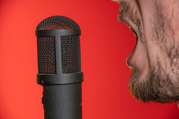 Singing Male Mouth In Front Of A Microphone On A Red Background. Broadcast, Radio and Podcasts. Singing Songs and Recording into the Microphone.
