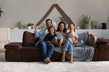 Portrait of happy family sitting on couch under cardboard roof, smiling overjoyed mother and father...