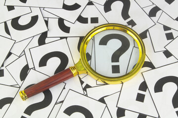 Magnifying glass on many question marks close-up