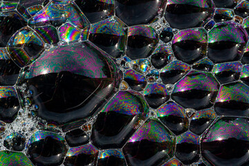 Close up, macro shot of a soap bubble, multicolored rainbow with yellow, purple, pink, blue and green colors on black background.