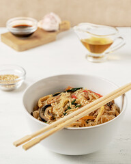chapchae - korean starch noodles in bowl with chopsticks