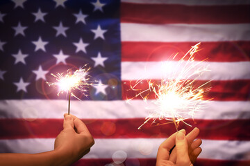 4th of July - Independence Day of USA. Women holding burning sparklers against American flag,...
