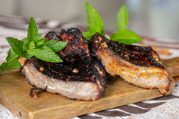 Grilled steak with mint stalks on wooden chopping board.