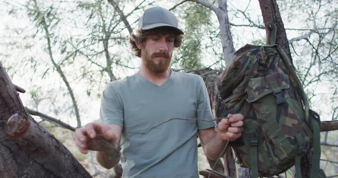 Bearded caucasian male survivalist untying paracord at camp in wilderness