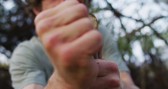 Bearded caucasian male survivalist tying paracord to branch to make a fire bow at camp in wilderness