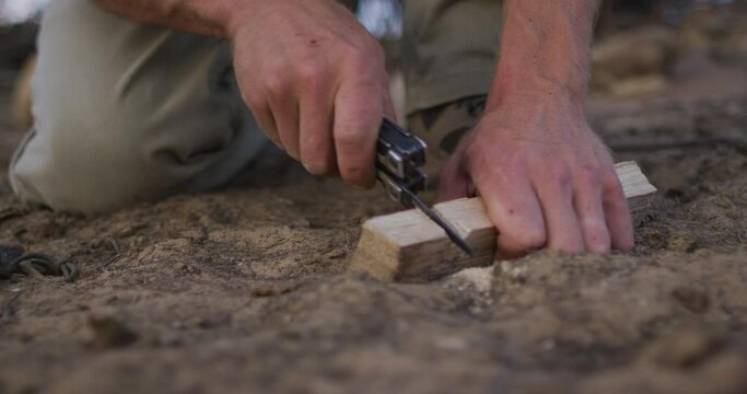 Caucasian male survivalist cutting notch in fireboard at camp in wilderness