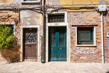 Fototapeta na wymiar Closed doors of ancient weathered brick wall residential houses with cables and pipes on exterior