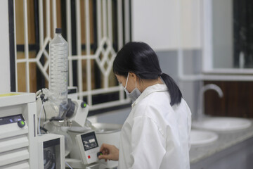 Asian woman scientist operating a rotary evaporator to make an experiment in the laboratory