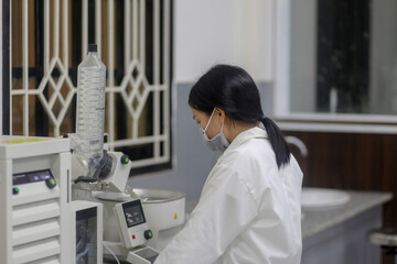 Vietnamese woman scientist operating a rotary evaporator to make an experiment in the laboratory