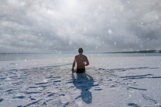 A tough man standing in an ice hole for having an ice bath in a frozen lake