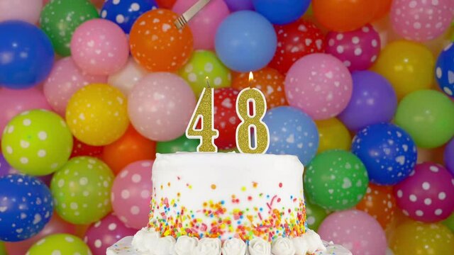 Cake with burning candles number 48. Celebration cake on a bright festive background of colorful balloons.