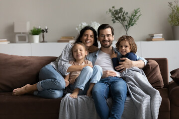 Portrait of happy family with two kids relaxing sitting on couch, smiling father in glasses with...