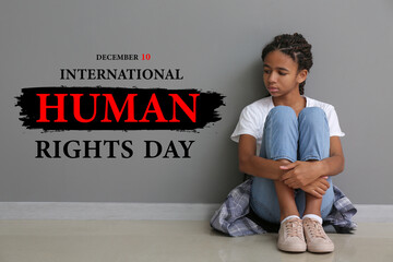 Sad African-American girl sitting near grey wall. International Day of Human Rights